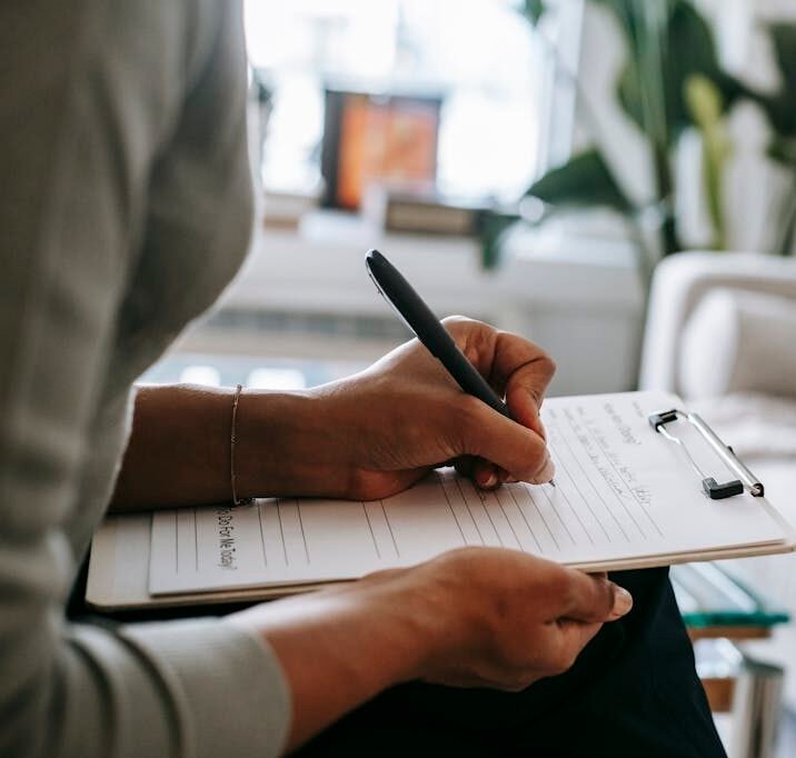 Unrecognizable ethnic female therapist taking notes on clipboard while filling out form during psychological appointment with anonymous client lying on blurred background